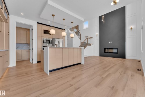 The property features light wood flooring, a kitchen island with pendant lighting, and a modern fireplace integrated into a dark accent wall - 503 Creekside Bay, Leduc, AB - Indoor Photo Showing Kitchen