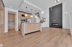 The property features light wood flooring, a kitchen island with pendant lighting, and a modern fireplace integrated into a dark accent wall - 