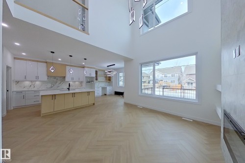 This open-concept living area features high ceilings, large windows, and light wood herringbone flooring - 8425 Mayday Link Link, Edmonton, AB - Indoor Photo Showing Kitchen