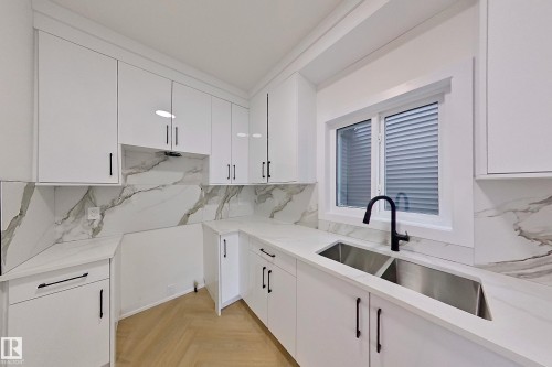 Modern kitchen featuring white cabinetry with black hardware, white countertops, and a white and grey veined backsplash - 8425 Mayday Link Link, Edmonton, AB - Indoor Photo Showing Kitchen