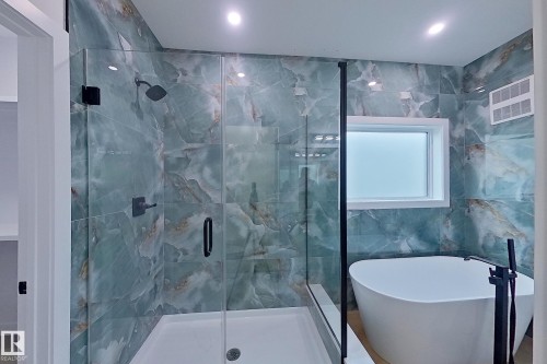 The bathroom features a spacious glass-enclosed shower with a dark-toned shower head and control, complemented by a freestanding soaking tub with a dark-toned floor-mounted faucet - 8425 Mayday Link Link, Edmonton, AB - Indoor Photo Showing Bathroom