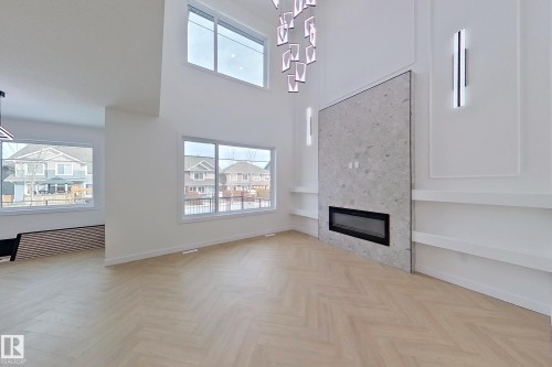 Spacious living area featuring light-toned chevron pattern flooring, a fireplace with a stone-look surround, and several windows providing natural light - 8425 Mayday Link Link, Edmonton, AB - Indoor Photo Showing Other Room