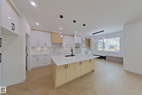 The kitchen features white cabinetry, a large kitchen island with a sink, and a white marble-patterned backsplash - 8425 Mayday Link Link, Edmonton, AB - Indoor Photo Showing Kitchen With Upgraded Kitchen
