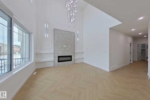 Spacious interior featuring chevron pattern flooring, a fireplace with a stone-look surround, and large windows - 8425 Mayday Link Link, Edmonton, AB - Indoor Photo Showing Other Room
