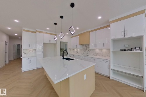 The kitchen features an expansive island with a white countertop and a black sink, complemented by white cabinetry and a marble-patterned backsplash - 8425 Mayday Link Link, Edmonton, AB - Indoor Photo Showing Kitchen With Upgraded Kitchen