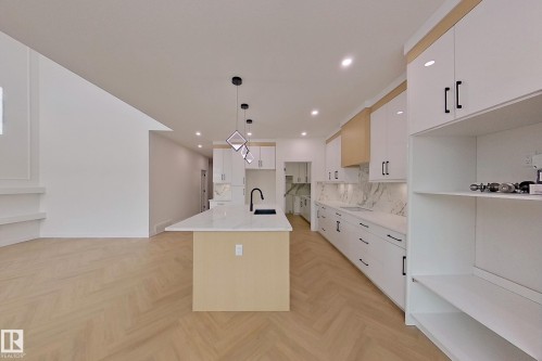 The kitchen features a large island with a sink, white cabinetry with black hardware, and a white marble-patterned backsplash - 8425 Mayday Link Link, Edmonton, AB - Indoor Photo Showing Kitchen