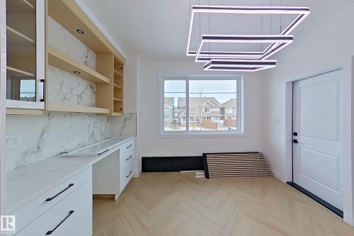 This area features a built-in desk and cabinetry with a marble-patterned backsplash, light wood open shelving, and a window providing natural light - 8425 Mayday Link Link, Edmonton, AB - Indoor Photo Showing Other Room