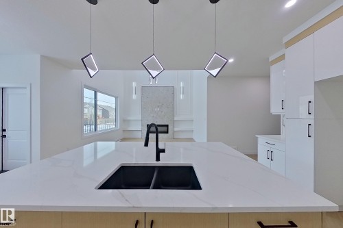 Kitchen featuring a white countertop with a black double sink and faucet, suspended light fixtures, and white cabinetry - 8425 Mayday Link Link, Edmonton, AB - Indoor Photo Showing Kitchen With Double Sink