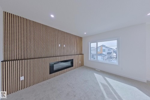 The room features a decorative slatted wood accent wall with an integrated linear electric fireplace - 8425 Mayday Link Link, Edmonton, AB - Indoor With Fireplace