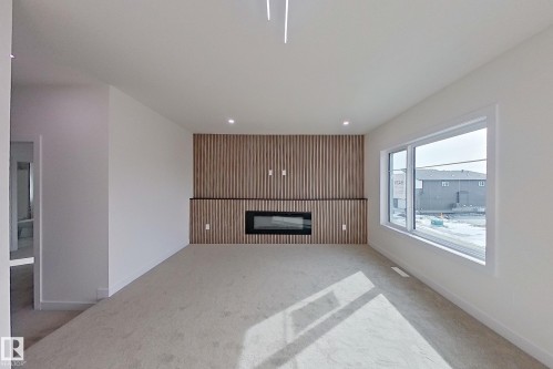 Living area featuring a modern electric fireplace with a wood-paneled accent wall, recessed lighting, and a large window providing natural light - 8425 Mayday Link Link, Edmonton, AB - Indoor With Fireplace
