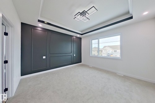 This room features a decorative accent wall with panel molding, a coffered ceiling with a modern light fixture, and light-colored carpeting - 8425 Mayday Link Link, Edmonton, AB - Indoor Photo Showing Other Room