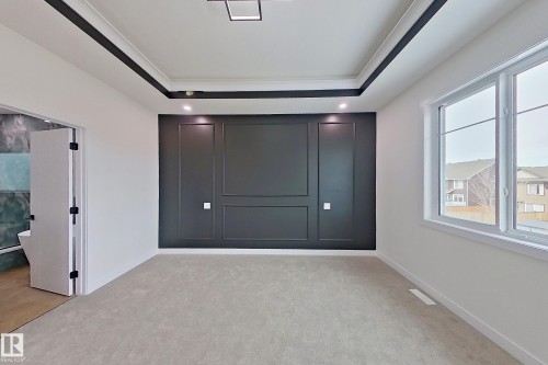 This room features a decorative accent wall with panel molding, a tray ceiling with recessed lighting, and a large window providing natural light - 8425 Mayday Link Link, Edmonton, AB - Indoor Photo Showing Other Room