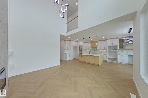 Open concept living space featuring high ceilings, light wood flooring with a herringbone pattern, and a modern kitchen with a large island and light-colored cabinetry - 8425 Mayday Link Link, Edmonton, AB - Indoor