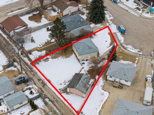 Aerial view of the property, featuring a main residence with a gray roof and light-colored siding, a detached garage with a pink and gray roof, and a large lot partially covered in snow - 9409 154 Street, Edmonton, AB - Outdoor With View