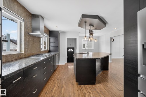 The kitchen features hardwood floors, dark cabinetry, and a central island with an integrated sink and pendant lighting - 3613 113 Avenue, Edmonton, AB - Indoor Photo Showing Kitchen With Upgraded Kitchen