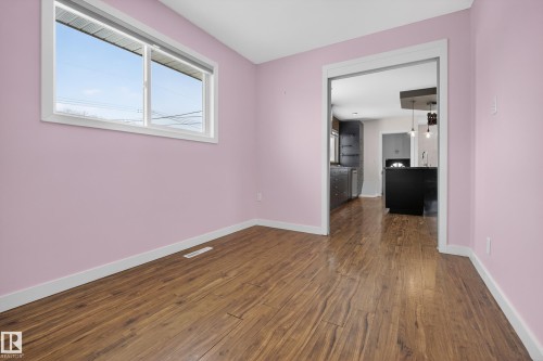 Room with wood style flooring and a window, featuring a doorway that leads to a kitchen area with dark cabinetry and a kitchen island - 3613 113 Avenue, Edmonton, AB - Indoor Photo Showing Other Room