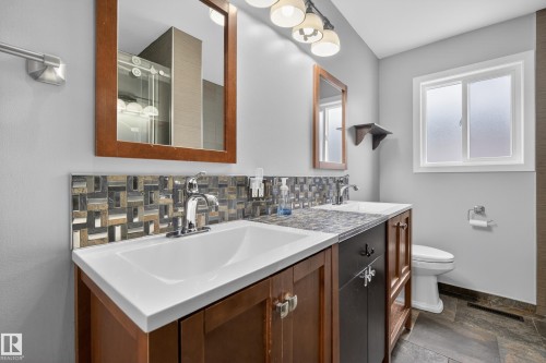 This bathroom features a double vanity with brown cabinetry and white sinks, complemented by a decorative tiled backsplash - 3613 113 Avenue, Edmonton, AB - Indoor Photo Showing Bathroom