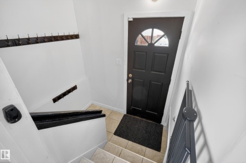 Entryway featuring a black door with an arched window, light tile flooring, and stairs with a black handrail - 3613 113 Avenue, Edmonton, AB - Indoor Photo Showing Other Room