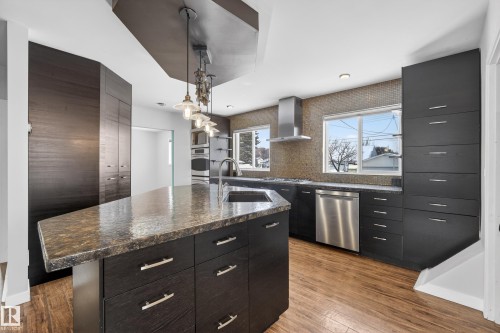The kitchen features dark cabinetry, a large kitchen island with a stone countertop, and stainless steel appliances - 3613 113 Avenue, Edmonton, AB - Indoor Photo Showing Kitchen With Upgraded Kitchen