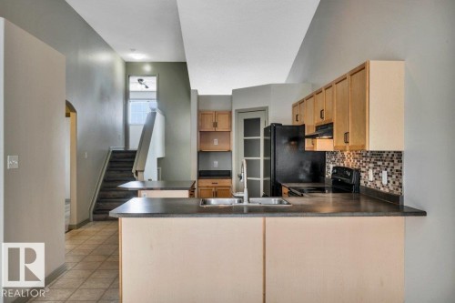The kitchen features light wood cabinetry, dark countertops, and a tiled backsplash - 902 Graham Wynd, Edmonton, AB - Indoor Photo Showing Kitchen