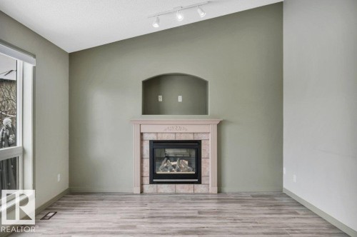 Living area featuring a fireplace with a stone surround and mantel, vaulted ceilings, track lighting, and wood-look flooring - 902 Graham Wynd, Edmonton, AB - Indoor With Fireplace