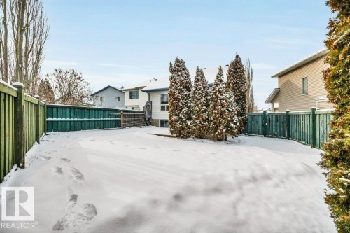 The property features a fenced yard with evergreen trees and a snow-covered lawn - 902 Graham Wynd, Edmonton, AB - Outdoor