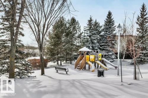 The property is located in a community with a playground featuring slides and climbing structures, surrounded by snow-covered evergreen trees and a park bench - 902 Graham Wynd, Edmonton, AB - Outdoor
