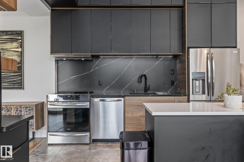 The kitchen features dark cabinetry, stainless steel appliances including a refrigerator, oven, and dishwasher, and a dark backsplash with light veining - 314 10309 107 Street, Edmonton, AB - Indoor Photo Showing Kitchen