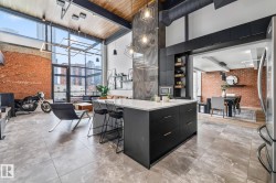 Contemporary open-concept living space featuring high ceilings with exposed ductwork, large windows, and a brick wall accent - 