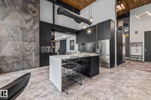 The modern kitchen features dark cabinetry, stainless steel appliances, a white island with seating, and geometric pendant lighting - 314 10309 107 Street, Edmonton, AB - Indoor Photo Showing Kitchen
