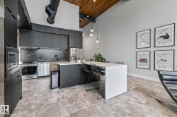 Modern kitchen featuring dark cabinetry, stainless steel appliances, and a kitchen island with seating - 