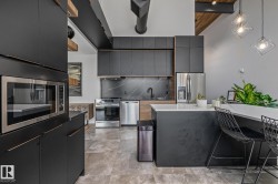 Modern kitchen featuring dark cabinetry, stainless steel appliances, and a kitchen island with a light-colored countertop - 