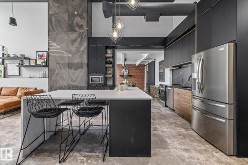 Modern kitchen featuring an island with a white countertop, stainless steel appliances, black cabinetry, and a dark tile backsplash - 314 10309 107 Street, Edmonton, AB - Indoor Photo Showing Kitchen