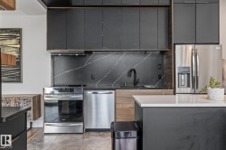 The kitchen features dark cabinetry, stainless steel appliances including a refrigerator, oven, and dishwasher, and a dark backsplash with light veining - 