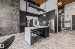 The modern kitchen features dark cabinetry, stainless steel appliances, a white island with seating, and geometric pendant lighting - 