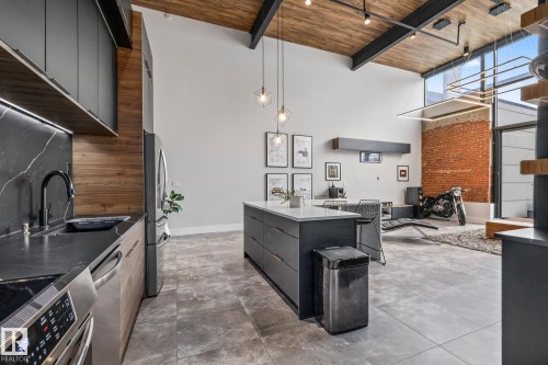 The open concept living area features a kitchen with dark cabinetry, stainless steel appliances, and a central island with a light-colored countertop - 314 10309 107 Street, Edmonton, AB - Indoor Photo Showing Kitchen