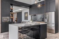 Modern kitchen featuring dark cabinetry, a white island with seating, stainless steel appliances, and geometric pendant lighting - 