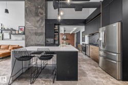 Modern kitchen featuring an island with a white countertop, stainless steel appliances, black cabinetry, and a dark tile backsplash - 