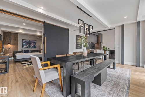 Open-concept living space with light hardwood flooring, a dining area featuring a dark wooden table and benches, and a modern kitchen with dark cabinetry and a tiled backsplash - 314 10309 107 Street, Edmonton, AB - Indoor
