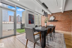 This dining area features an exposed brick accent wall, light wood flooring, and a contemporary chandelier - 