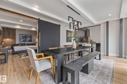 Open-concept living space with light hardwood flooring, a dining area featuring a dark wooden table and benches, and a modern kitchen with dark cabinetry and a tiled backsplash - 