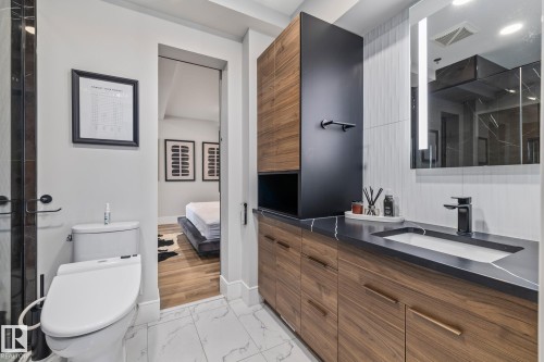 This bathroom features a contemporary vanity with a dark countertop and an integrated sink, complemented by a black faucet and a wall-mounted mirror with integrated lighting - 314 10309 107 Street, Edmonton, AB - Indoor Photo Showing Bathroom