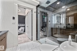 Contemporary bathroom featuring a spacious glass-enclosed shower with dark marble-style tiling, a vanity with a dark countertop and wooden cabinetry, and white tiled walls - 