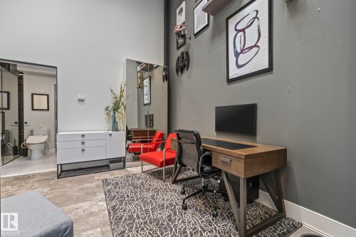 This versatile space features a dedicated office area with a desk, a large wall-mounted mirror, and a sleek white cabinet - 314 10309 107 Street, Edmonton, AB - Indoor