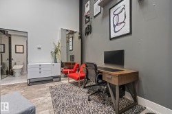 This versatile space features a dedicated office area with a desk, a large wall-mounted mirror, and a sleek white cabinet - 