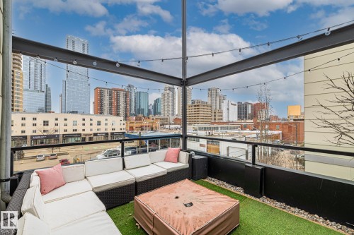 The property features an outdoor patio with artificial turf, string lighting, and glass railings, offering views of the surrounding buildings - 314 10309 107 Street, Edmonton, AB - Outdoor With Deck Patio Veranda