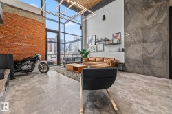 The living area features floor-to-ceiling windows, exposed brick accents, and a distinctive high ceiling - 