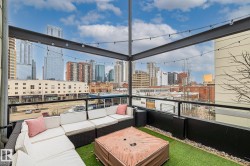 The property features an outdoor patio with artificial turf, string lighting, and glass railings, offering views of the surrounding buildings - 
