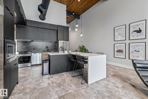 Modern kitchen featuring dark cabinetry, stainless steel appliances, and a kitchen island with seating - 314 10309 107 Street, Edmonton, AB - Indoor Photo Showing Kitchen