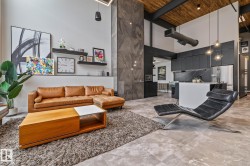 This open concept living area showcases high ceilings with exposed beams, large format floor tiling, and a contemporary kitchen with dark cabinetry and stainless steel appliances - 